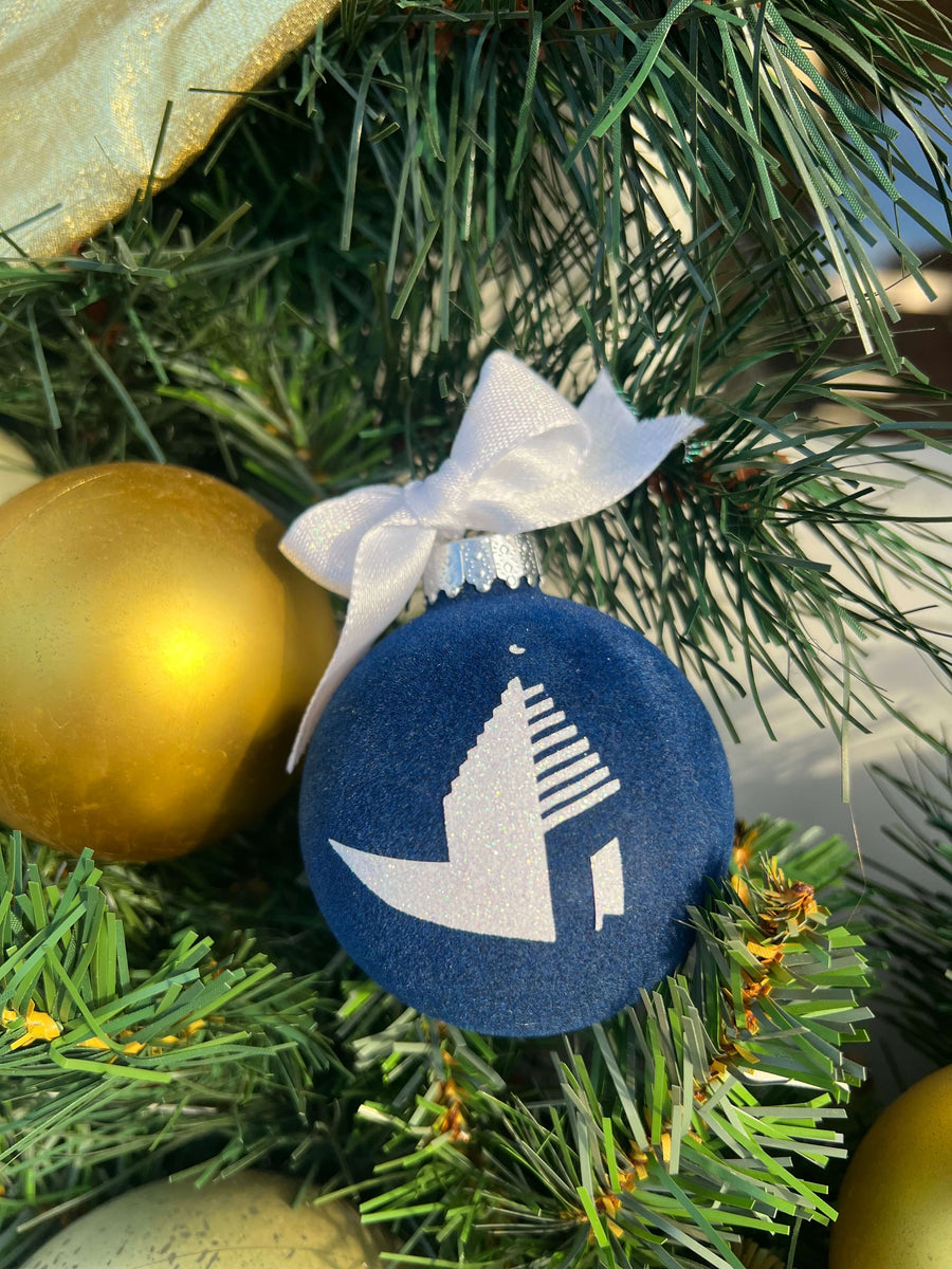 Decorative ornament with a white house silhouette on a blue background, hanging on a Christmas tree.
